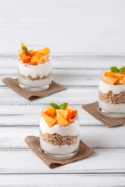 Trabzon hurması kremalı pasta ister güzel gözlük, taze olgun meyve dilimleri Beyaz ahşap zemin üzerinde. Sağlıklı vejetaryen yemek. Lezzetli tatlı. Fotoğraf kadar kapatın. Seçici odak.