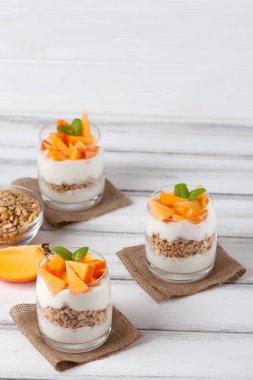 Trabzon hurması kremalı pasta ister güzel gözlük, taze olgun meyve dilimleri Beyaz ahşap zemin üzerinde. Sağlıklı vejetaryen yemek. Lezzetli tatlı. Fotoğraf kadar kapatın. Seçici odak.