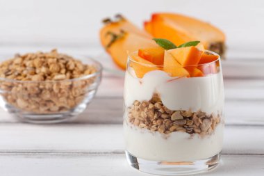 Trabzon hurması kremalı pasta ister güzel gözlük, taze olgun meyve dilimleri Beyaz ahşap zemin üzerinde. Sağlıklı vejetaryen yemek. Lezzetli tatlı. Fotoğraf kadar kapatın. Seçici odak.