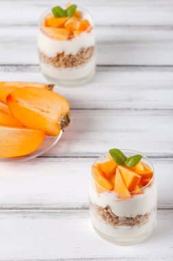 Trabzon hurması kremalı pasta ister güzel gözlük, taze olgun meyve dilimleri Beyaz ahşap zemin üzerinde. Sağlıklı vejetaryen yemek. Lezzetli tatlı. Fotoğraf kadar kapatın. Seçici odak.