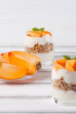 Trabzon hurması kremalı pasta ister güzel gözlük, taze olgun meyve dilimleri Beyaz ahşap zemin üzerinde. Sağlıklı vejetaryen yemek. Lezzetli tatlı. Fotoğraf kadar kapatın. Seçici odak.