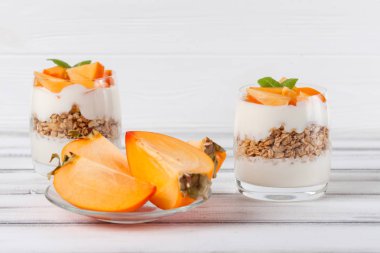 Trabzon hurması kremalı pasta ister güzel gözlük, taze olgun meyve dilimleri Beyaz ahşap zemin üzerinde. Sağlıklı vejetaryen yemek. Lezzetli tatlı. Fotoğraf kadar kapatın. Seçici odak.