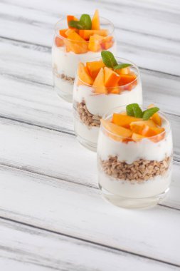 Trabzon hurması kremalı pasta ister güzel gözlük, taze olgun meyve dilimleri Beyaz ahşap zemin üzerinde. Sağlıklı vejetaryen yemek. Lezzetli tatlı. Fotoğraf kadar kapatın. Seçici odak.