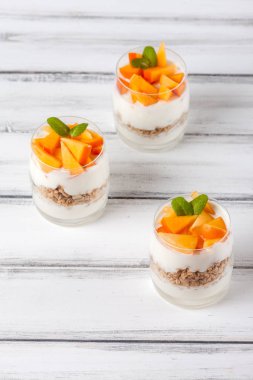 Trabzon hurması kremalı pasta ister güzel gözlük, taze olgun meyve dilimleri Beyaz ahşap zemin üzerinde. Sağlıklı vejetaryen yemek. Lezzetli tatlı. Fotoğraf kadar kapatın. Seçici odak.