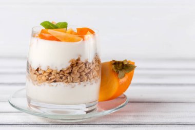 Trabzon hurması kremalı pasta ister güzel gözlük, taze olgun meyve dilimleri Beyaz ahşap zemin üzerinde. Sağlıklı vejetaryen yemek. Lezzetli tatlı. Fotoğraf kadar kapatın. Seçici odak.