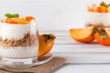 Trabzon hurması kremalı pasta ister güzel gözlük, taze olgun meyve dilimleri Beyaz ahşap zemin üzerinde. Sağlıklı vejetaryen yemek. Lezzetli tatlı. Fotoğraf kadar kapatın. Seçici odak.