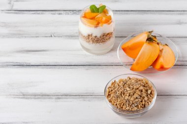 Trabzon hurması kremalı pasta ister güzel gözlük, taze olgun meyve dilimleri Beyaz ahşap zemin üzerinde. Sağlıklı vejetaryen yemek. Lezzetli tatlı. Fotoğraf kadar kapatın. Seçici odak.