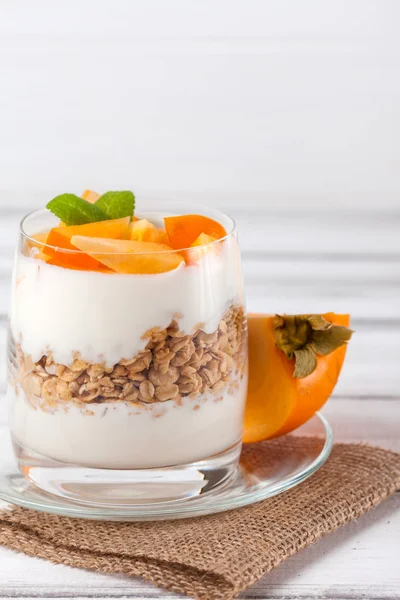 Persimmon creamy trifle in beautiful glasses, fresh ripe fruit slices on white wooden background. Healthy vegetarian food. Delicious dessert. Close up photography. Selective focus. — Stock Photo, Image