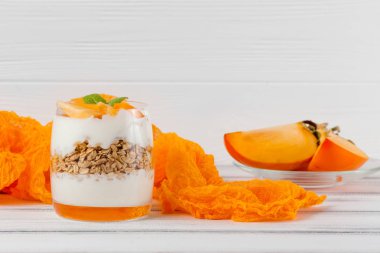 Trabzon hurması kremalı pasta ister güzel gözlük, taze olgun meyve dilimleri Beyaz ahşap zemin üzerinde. Sağlıklı vejetaryen yemek. Lezzetli tatlı. Fotoğraf kadar kapatın. Seçici odak.