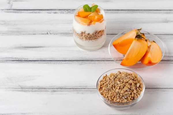 Trabzon hurması kremalı pasta ister güzel gözlük, taze olgun meyve dilimleri Beyaz ahşap zemin üzerinde. Sağlıklı vejetaryen yemek. Lezzetli tatlı. Fotoğraf kadar kapatın. Seçici odak.