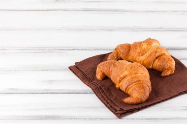 Taze pişmiş kruvasanlar beyaz eski ahşap zemin üzerinde kahverengi peçete üzerinde. Kahvaltı için taze hamur işleri. Lezzetli tatlı. Portre fotoğrafçılığı. Seçici odak. Yatay başlık