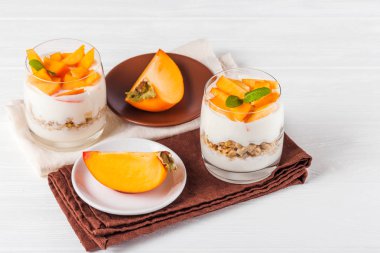 Persimmon creamy trifle in beautiful glasses, fresh ripe fruit slices on white wooden background. Healthy vegetarian food. Delicious dessert. Close up photography. Selective focus. clipart