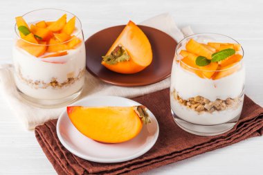 Trabzon hurması kremalı pasta ister güzel gözlük, taze olgun meyve dilimleri Beyaz ahşap zemin üzerinde. Sağlıklı vejetaryen yemek. Lezzetli tatlı. Fotoğraf kadar kapatın. Seçici odak.