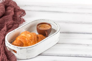 Taze pişmiş kruvasanlar üzerinde kahverengi peçete, krem, kahve Beyaz ahşap zemin üzerinde seramik yemekler için. Kahvaltı için taze hamur işleri. Lezzetli tatlı. Portre fotoğrafçılığı. Yatay başlık