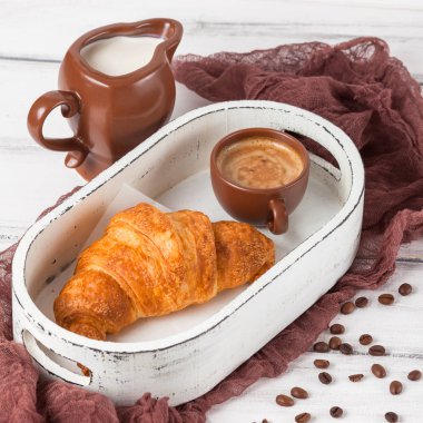 Taze pişmiş kruvasanlar üzerinde kahverengi peçete, krem, kahve Beyaz ahşap zemin üzerinde seramik yemekler için. Kahvaltı için taze hamur işleri. Lezzetli tatlı. Portre fotoğrafçılığı. Yatay başlık