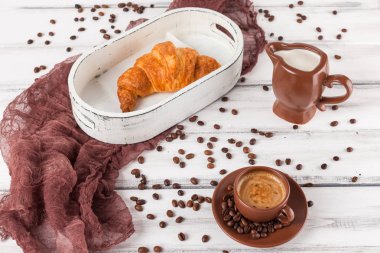 Taze pişmiş kruvasanlar üzerinde kahverengi peçete, krem, kahve Beyaz ahşap zemin üzerinde seramik yemekler için. Kahvaltı için taze hamur işleri. Lezzetli tatlı. Portre fotoğrafçılığı. Yatay başlık