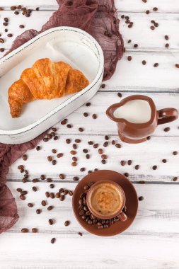 Taze pişmiş kruvasanlar üzerinde kahverengi peçete, krem, kahve Beyaz ahşap zemin üzerinde seramik yemekler için. Kahvaltı için taze hamur işleri. Lezzetli tatlı. Portre fotoğrafçılığı. Dikey başlık