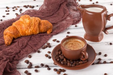 Taze pişmiş kruvasanlar üzerinde kahverengi peçete, krem, kahve Beyaz ahşap zemin üzerinde seramik yemekler için. Kahvaltı için taze hamur işleri. Lezzetli tatlı. Portre fotoğrafçılığı. Yatay başlık