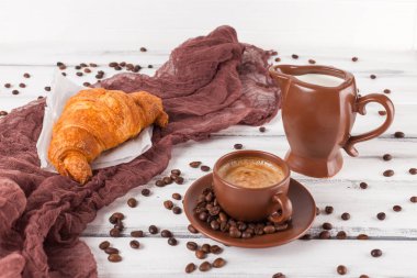 Taze pişmiş kruvasanlar üzerinde kahverengi peçete, krem, kahve Beyaz ahşap zemin üzerinde seramik yemekler için. Kahvaltı için taze hamur işleri. Lezzetli tatlı. Portre fotoğrafçılığı. Yatay başlık