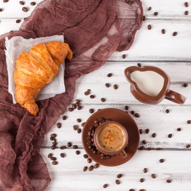 Taze pişmiş kruvasanlar üzerinde kahverengi peçete, krem, kahve Beyaz ahşap zemin üzerinde seramik yemekler için. Kahvaltı için taze hamur işleri. Lezzetli tatlı. Portre fotoğrafçılığı. Yatay başlık