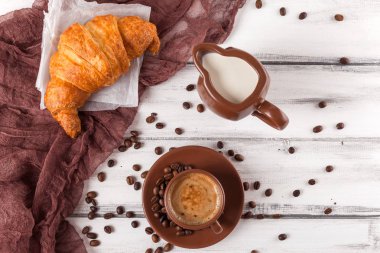 Taze pişmiş kruvasanlar üzerinde kahverengi peçete, krem, kahve Beyaz ahşap zemin üzerinde seramik yemekler için. Kahvaltı için taze hamur işleri. Lezzetli tatlı. Portre fotoğrafçılığı. Yatay başlık