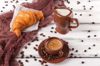 Taze pişmiş kruvasanlar üzerinde kahverengi peçete, krem, kahve Beyaz ahşap zemin üzerinde seramik yemekler için. Kahvaltı için taze hamur işleri. Lezzetli tatlı. Portre fotoğrafçılığı. Yatay başlık