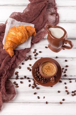 Taze pişmiş kruvasanlar üzerinde kahverengi peçete, krem, kahve Beyaz ahşap zemin üzerinde seramik yemekler için. Kahvaltı için taze hamur işleri. Lezzetli tatlı. Portre fotoğrafçılığı. Dikey başlık