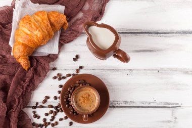 Taze pişmiş kruvasanlar üzerinde kahverengi peçete, krem, kahve Beyaz ahşap zemin üzerinde seramik yemekler için. Kahvaltı için taze hamur işleri. Lezzetli tatlı. Portre fotoğrafçılığı. Yatay başlık