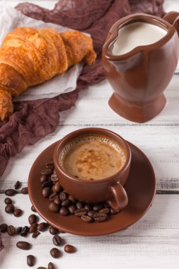 Taze pişmiş kruvasanlar üzerinde kahverengi peçete, krem, kahve Beyaz ahşap zemin üzerinde seramik yemekler için. Kahvaltı için taze hamur işleri. Lezzetli tatlı. Portre fotoğrafçılığı. Dikey başlık