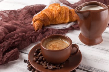 Taze pişmiş kruvasanlar üzerinde kahverengi peçete, krem, kahve Beyaz ahşap zemin üzerinde seramik yemekler için. Kahvaltı için taze hamur işleri. Lezzetli tatlı. Portre fotoğrafçılığı. Yatay başlık