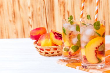 Buz ve nane yaprakları ile şeftali limonata. Ev yapımı limonata, beyaz ve turuncu olgun olgun nektarin. Şeftali çay iki kadeh. Beyaz ahşap zemin üzerinde serinletici yaz içeceği.