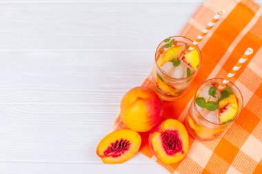 Buz ve nane yaprakları ile şeftali limonata. Ev yapımı limonata, beyaz ve turuncu olgun olgun nektarin. Şeftali çay iki kadeh. Beyaz ahşap zemin üzerinde serinletici yaz içeceği.