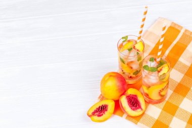 Buz ve nane yaprakları ile şeftali limonata. Ev yapımı limonata, beyaz ve turuncu olgun olgun nektarin. Şeftali çay iki kadeh. Beyaz ahşap zemin üzerinde serinletici yaz içeceği.