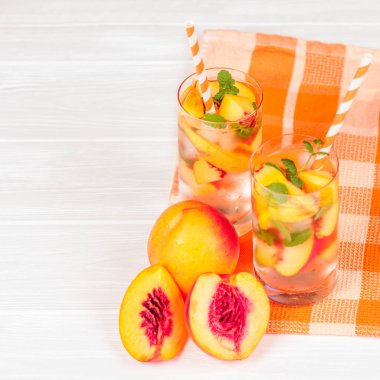 Buz ve nane yaprakları ile şeftali limonata. Ev yapımı limonata, beyaz ve turuncu olgun olgun nektarin. Şeftali çay iki kadeh. Beyaz ahşap zemin üzerinde serinletici yaz içeceği.