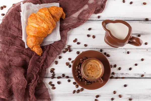 Freshly baked croissants on brown napkin, cream, to cups of coffee in ceramic dishes on white wooden background. Fresh pastries for breakfast. Delicious dessert. Closeup photography.Horizontal banner — Stock Photo, Image