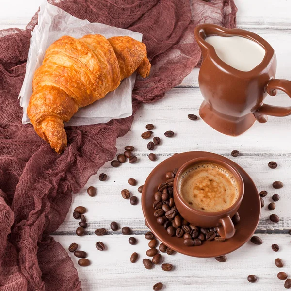 Taze pişmiş kruvasanlar üzerinde kahverengi peçete, krem, kahve Beyaz ahşap zemin üzerinde seramik yemekler için. Kahvaltı için taze hamur işleri. Lezzetli tatlı. Portre fotoğrafçılığı. Yatay başlık