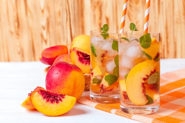 Buz ve nane yaprakları ile şeftali limonata. Ev yapımı limonata, beyaz ve turuncu olgun olgun nektarin. Şeftali çay iki kadeh. Beyaz ahşap zemin üzerinde serinletici yaz içeceği.