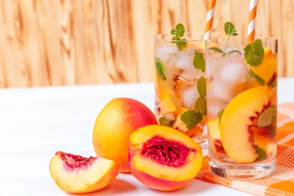 Buz ve nane yaprakları ile şeftali limonata. Ev yapımı limonata, beyaz ve turuncu olgun olgun nektarin. Şeftali çay iki kadeh. Beyaz ahşap zemin üzerinde serinletici yaz içeceği.