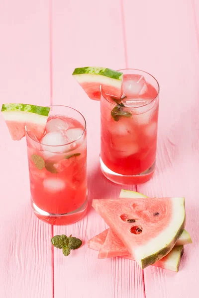 Watermelon lemonade with ice and mint leaves. Homemade lemonade of ripe berry with red and green ripes. Glass of cold watermelon tea. Refreshing summer drink. Cocktail on a wooden background — Stock Photo, Image