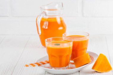 Güzel gözlük ve sürahi beyaz ahşap zemin üzerinde olgun sebze parçaları ile kabak taze meyve suyu. Tatlı portakal suyu. Sağlıklı beslenme, diyet Tema. Fotoğraf kadar kapatın. Yatay başlık