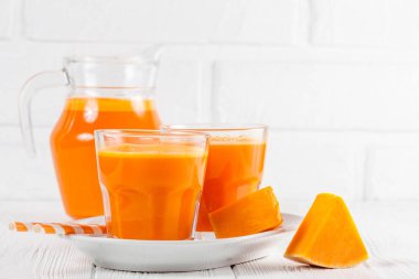 Güzel gözlük ve sürahi beyaz ahşap zemin üzerinde olgun sebze parçaları ile kabak taze meyve suyu. Tatlı portakal suyu. Sağlıklı beslenme, diyet Tema. Fotoğraf kadar kapatın. Yatay başlık