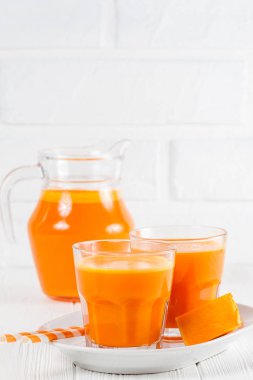 Güzel gözlük ve sürahi beyaz ahşap zemin üzerinde olgun sebze parçaları ile kabak taze meyve suyu. Tatlı portakal suyu. Sağlıklı beslenme, diyet Tema. Fotoğraf kadar kapatın. Dikey başlık