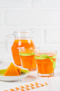 Güzel gözlük ve sürahi beyaz ahşap zemin üzerinde olgun sebze parçaları ile kabak taze meyve suyu. Tatlı portakal suyu. Sağlıklı beslenme, diyet Tema. Fotoğraf kadar kapatın. Dikey başlık