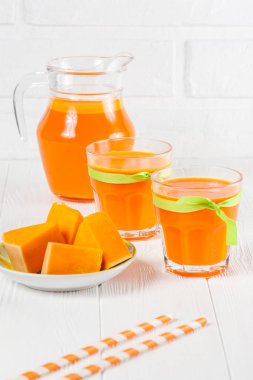 Güzel gözlük ve sürahi beyaz ahşap zemin üzerinde olgun sebze parçaları ile kabak taze meyve suyu. Tatlı portakal suyu. Sağlıklı beslenme, diyet Tema. Fotoğraf kadar kapatın. Dikey başlık