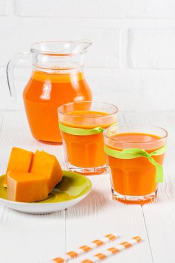 Güzel gözlük ve sürahi beyaz ahşap zemin üzerinde olgun sebze parçaları ile kabak taze meyve suyu. Tatlı portakal suyu. Sağlıklı beslenme, diyet Tema. Fotoğraf kadar kapatın. Dikey başlık