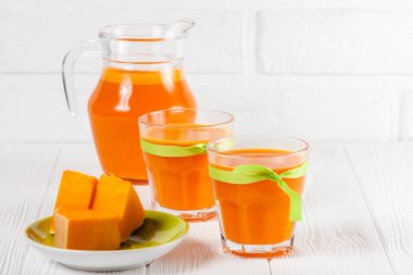 Güzel gözlük ve sürahi beyaz ahşap zemin üzerinde olgun sebze parçaları ile kabak taze meyve suyu. Tatlı portakal suyu. Sağlıklı beslenme, diyet Tema. Fotoğraf kadar kapatın. Yatay başlık