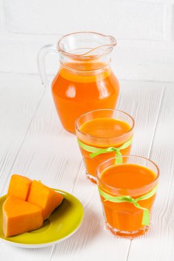 Güzel gözlük ve sürahi beyaz ahşap zemin üzerinde olgun sebze parçaları ile kabak taze meyve suyu. Tatlı portakal suyu. Sağlıklı beslenme, diyet Tema. Fotoğraf kadar kapatın. Dikey başlık