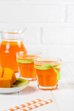 Güzel gözlük ve sürahi beyaz ahşap zemin üzerinde olgun sebze parçaları ile kabak taze meyve suyu. Tatlı portakal suyu. Sağlıklı beslenme, diyet Tema. Fotoğraf kadar kapatın. Dikey başlık