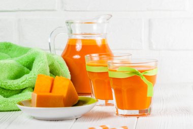 Güzel gözlük ve sürahi beyaz ahşap zemin üzerinde olgun sebze parçaları ile kabak taze meyve suyu. Tatlı portakal suyu. Sağlıklı beslenme, diyet Tema. Fotoğraf kadar kapatın. Yatay başlık