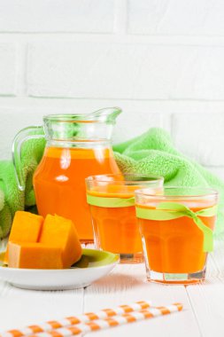 Güzel gözlük ve sürahi beyaz ahşap zemin üzerinde olgun sebze parçaları ile kabak taze meyve suyu. Tatlı portakal suyu. Sağlıklı beslenme, diyet Tema. Fotoğraf kadar kapatın. Dikey başlık